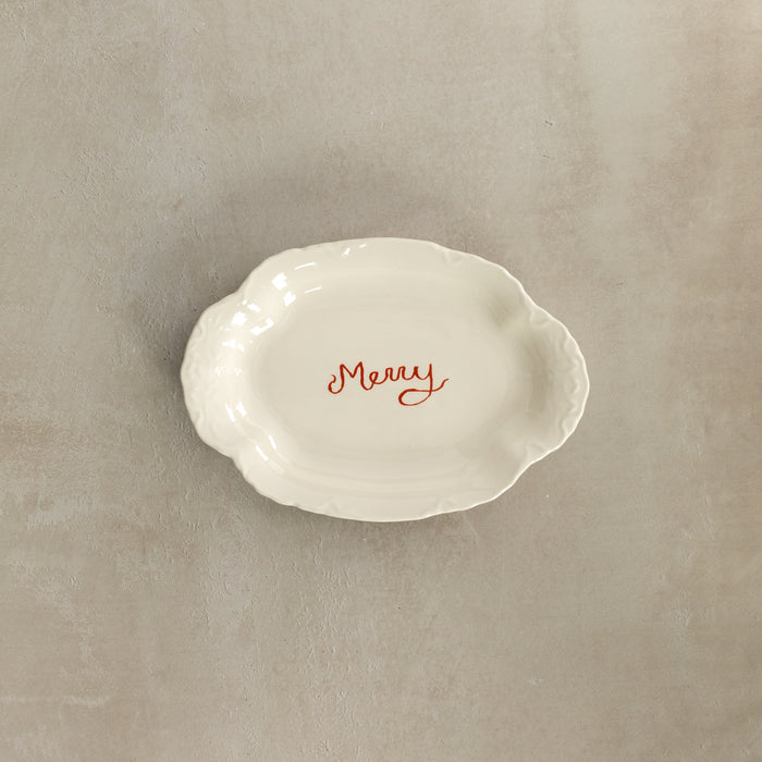 White ceramic dish with 'Merry' text on a beige background