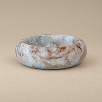 A polished stone dish with a marbled pattern of light blue, white, and brown, displayed on a solid beige background.