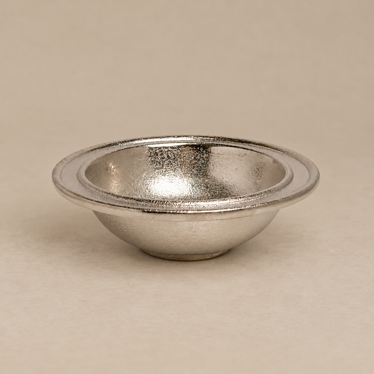 A small metallic silver bowl with a textured, hammered finish, shown on a neutral beige background.
