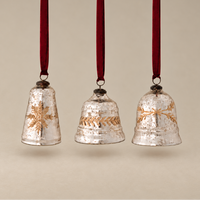 Three vintage-style hanging Christmas bells with a textured silver finish and gold decorative motifs, suspended by dark red ribbons against a warm beige background.