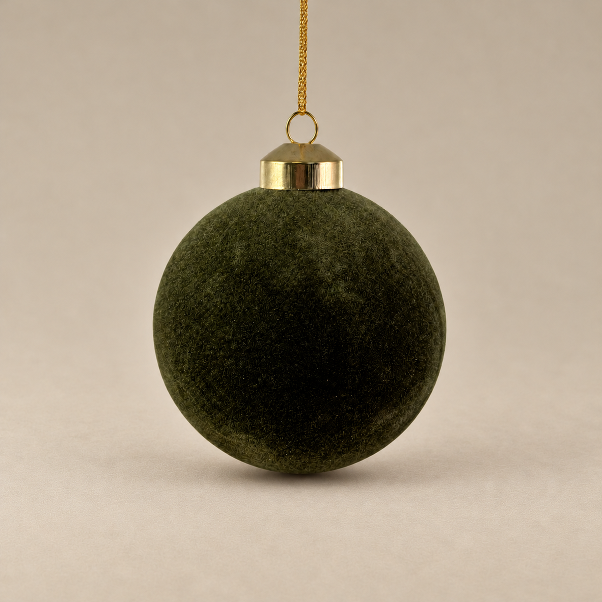 A dark olive green velvet Christmas ornament hanging from a gold metal cap and gold string against a neutral beige background.