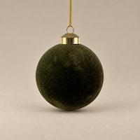 A dark olive green velvet Christmas ornament hanging from a gold metal cap and gold string against a neutral beige background.