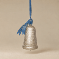 A textured silver bell ornament hanging from a blue velvet ribbon bow against a warm beige background.