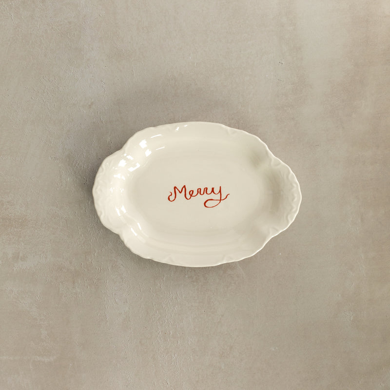 White ceramic dish with 'Merry' text on a beige background