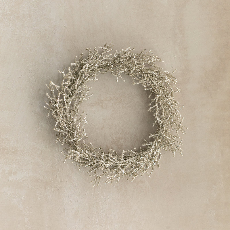 Decorative wreath with glittery branches on a beige wall